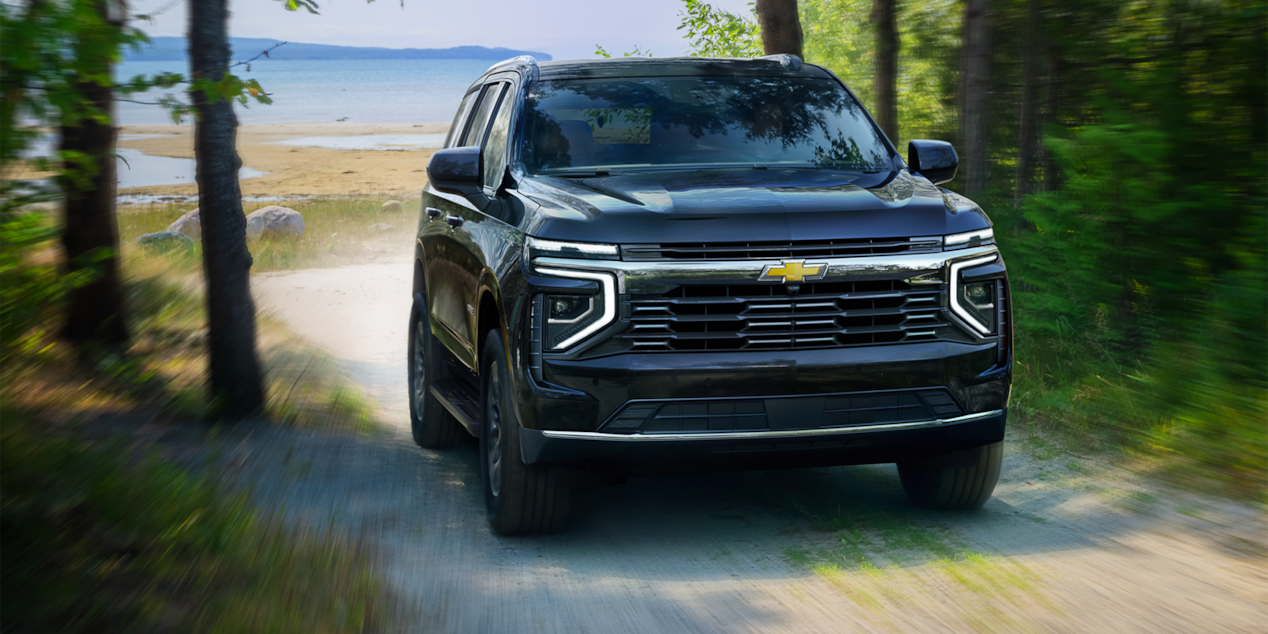 Vista frontal de tres cuartos de la SUV Chevrolet Tahoe 2025 circulando por un camino de tierra rodeado de árboles