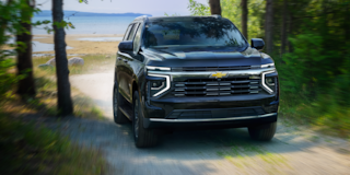 Vista frontal de tres cuartos de la SUV Chevrolet Tahoe 2025 circulando por un camino de tierra rodeado de árboles