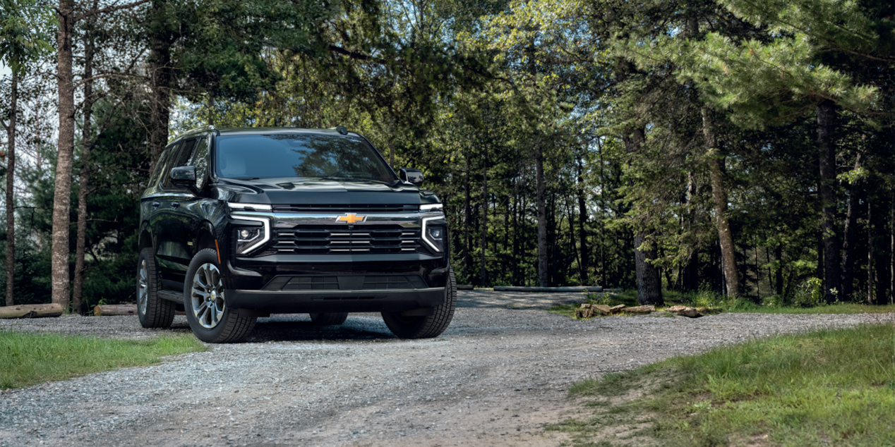 Vista delantera de tres cuartos de la SUV Chevrolet Suburban 2025 estacionada en un área boscosa
