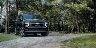 Vista delantera de tres cuartos de la SUV Chevrolet Suburban 2025 estacionada en un área boscosa