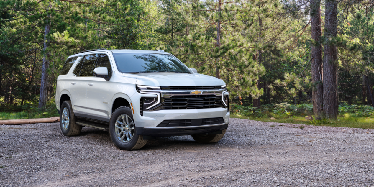 Vista delantera de tres cuartos de la SUV Chevrolet Suburban 2025 estacionada en un área boscosa