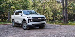 Vista delantera de tres cuartos de la SUV Chevrolet Suburban 2025 estacionada en un área boscosa
