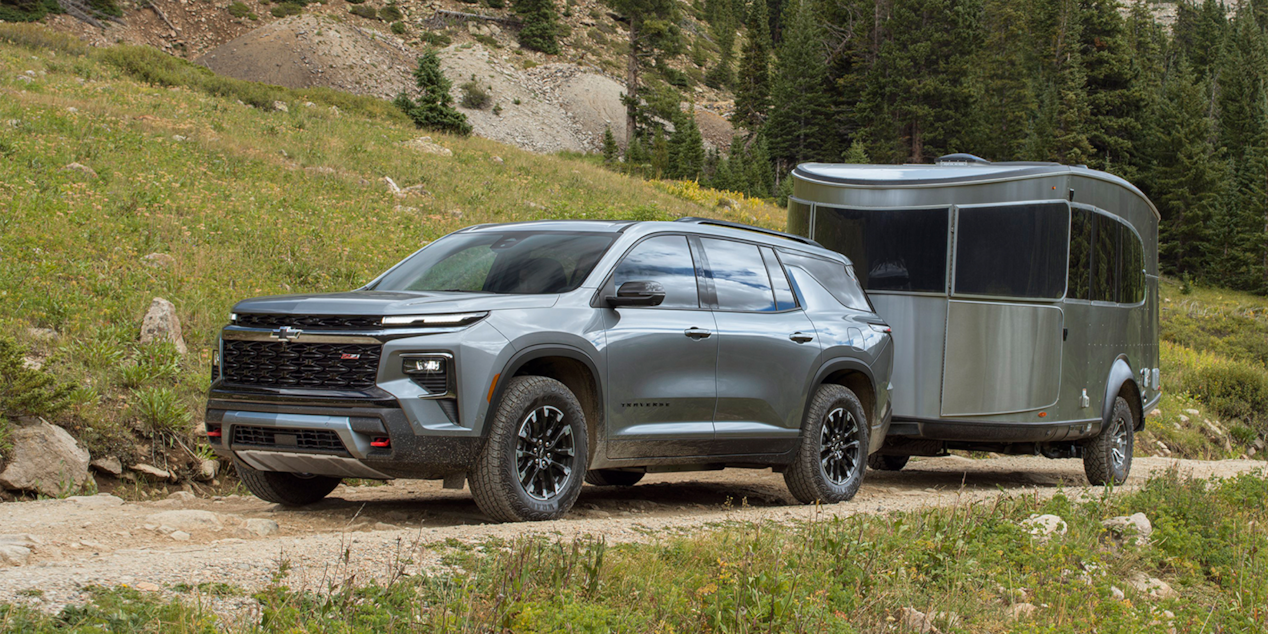 Three Quarters View of a Silver 2025 Chevy Traverse Pulling a Trailer with Grassy Plain on the Sides of the Road