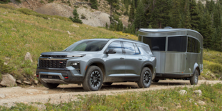Three Quarters View of a Silver 2025 Chevy Traverse Pulling a Trailer with Grassy Plain on the Sides of the Road