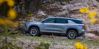 Side View of a Silver 2025 Chevy Traverse Driving Down a Road with a Mountain Wall to the Side