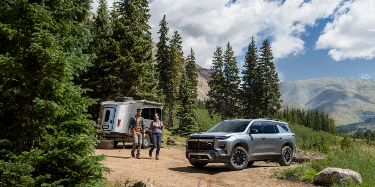 Three Quarters View of a Silver Chevy Traverse with a Man and a Woman Walking in Front of a Trailer