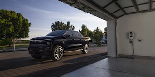 A black 2025 Silverado EV next to a garage getting charged with sunlight coming from the rear
