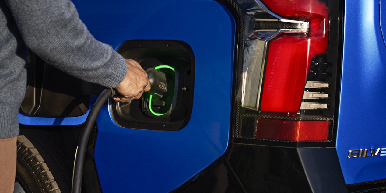 A person plugging in a charger to a 2025 blue Chevy Silverado EV