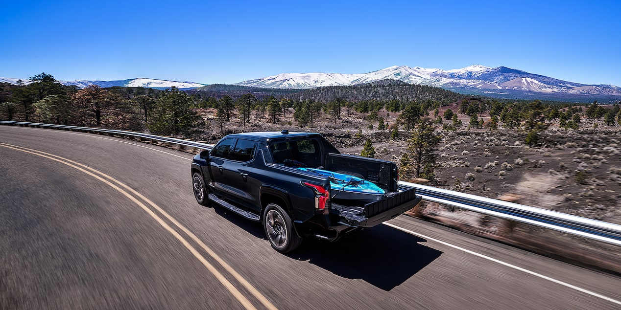 Rear three quarters view of a Chevy 2025 Silverado EV driving on the road next to mountains