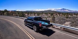 Rear three quarters view of a Chevy 2025 Silverado EV driving on the road next to mountains