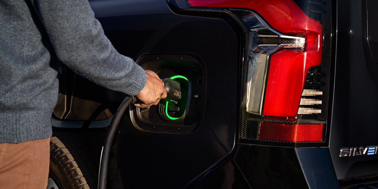A person plugging in a charger to a 2025 black Chevy Silverado EV