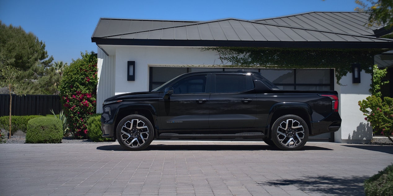 Side view of a black Chevy Silverado EV next to a house surrounded by trees
