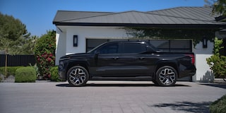 Side view of a black Chevy Silverado EV next to a house surrounded by trees