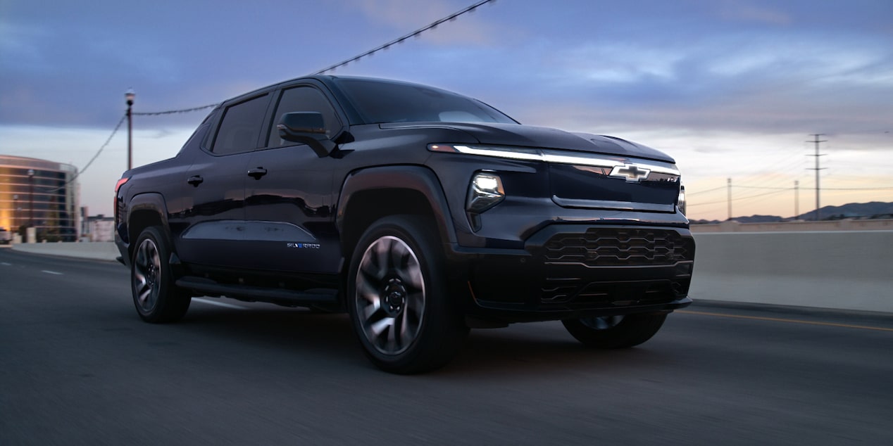 Low three quarter view of a black 2025 Silverado EV on a road with evening sky above