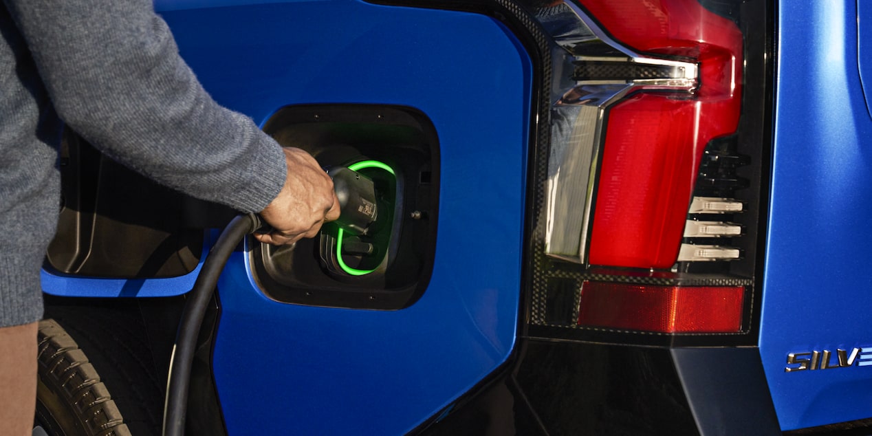 A person plugging in a charger to a 2025 blue Chevy Silverado EV