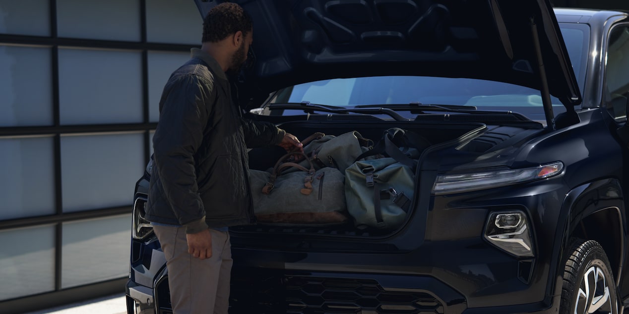 A man is putting his bags and belonging in the trunk of a black 2025 Chevy Silverado EV