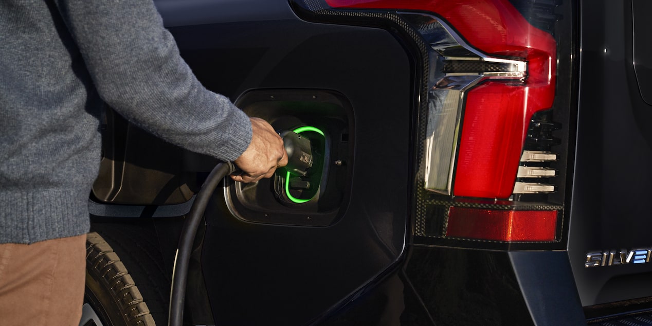 A person plugging in a charger to a 2025 black Chevy Silverado EV