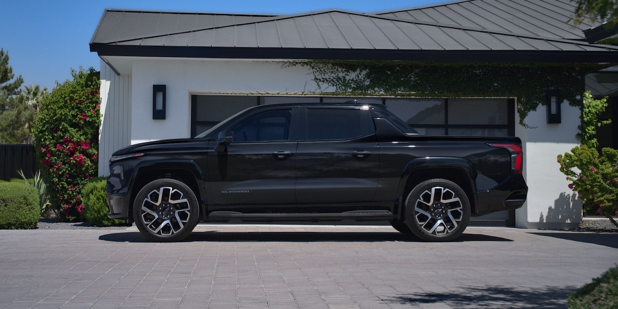 Side view of a black Chevy Silverado EV next to a house surrounded by trees