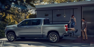 Side View of a Silver Chevy Silverado with a Woman on the Trunk and the Man behind Her