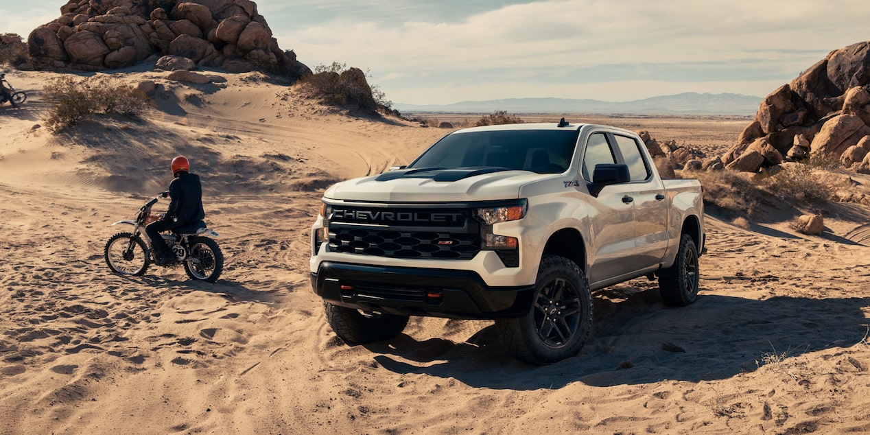 A Three Quarters View of a White Silverado Next to a Motorcycle on a Desert