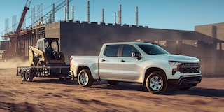 Three Quarters View of a White 2025 Chevy Silverado Pickup Truck Pulling a Skid Steer Loader on a Construction Site