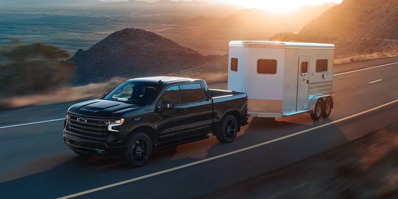 A Black 2025 Chevy Silverado Pickup Truck Pulling a Trailer with Sunlight from the Back