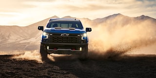 Front View of a 2025 Chevy Silverado Pickup Truck Kicking up Dirt with a Sunrise in the Back