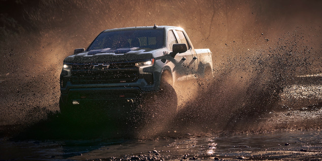 Three Quarters View of a Cypress Gray Chevy Silverado Pickup Truck kicking up mud