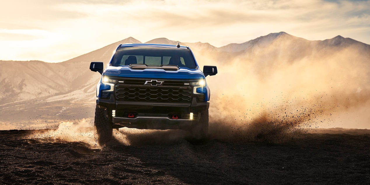 Front View of a 2025 Chevy Silverado Pickup Truck Kicking up Dirt with a Sunrise in the Back