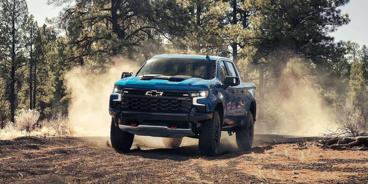 Three Quarters View of a Blue 2025 Chevy Silverado Pickup Truck Driving Down a Dirt Road