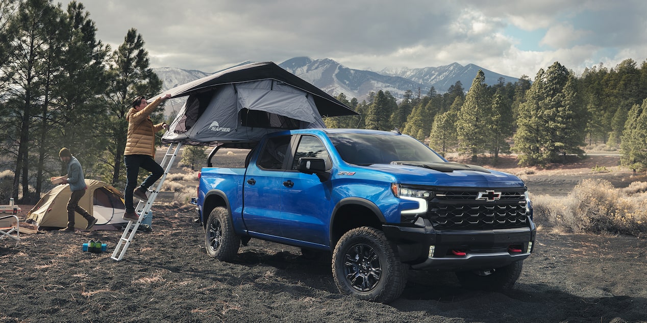 Three Quarters View of a Blue Chevy Silverado with a Man Building a Tent for Camping