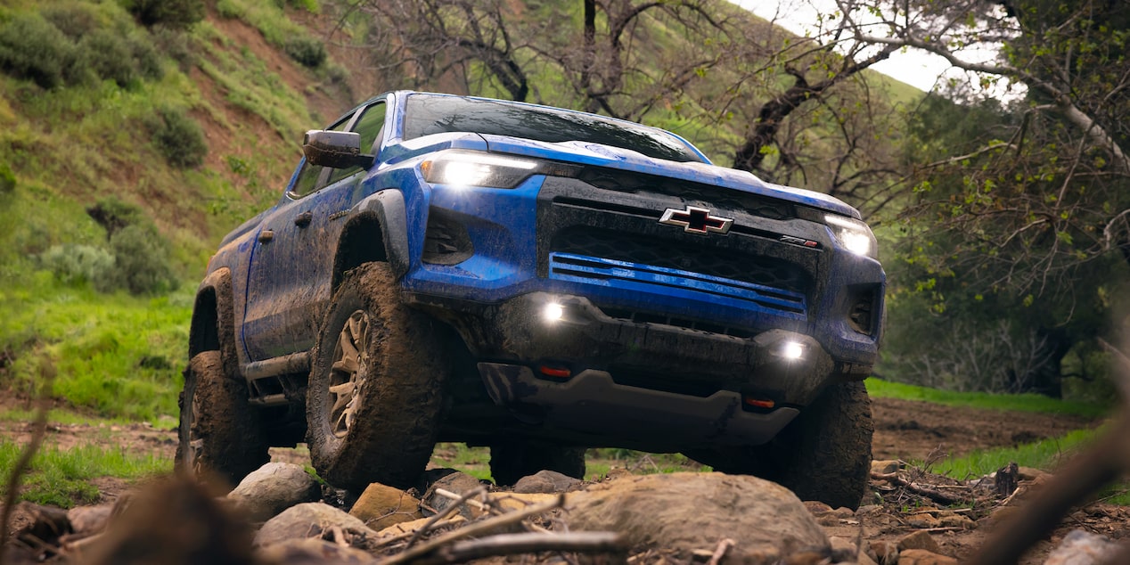 Low Angle Front View of a 2026 Blue Chevy Colorado Going Down a Rocky Road in a Forest