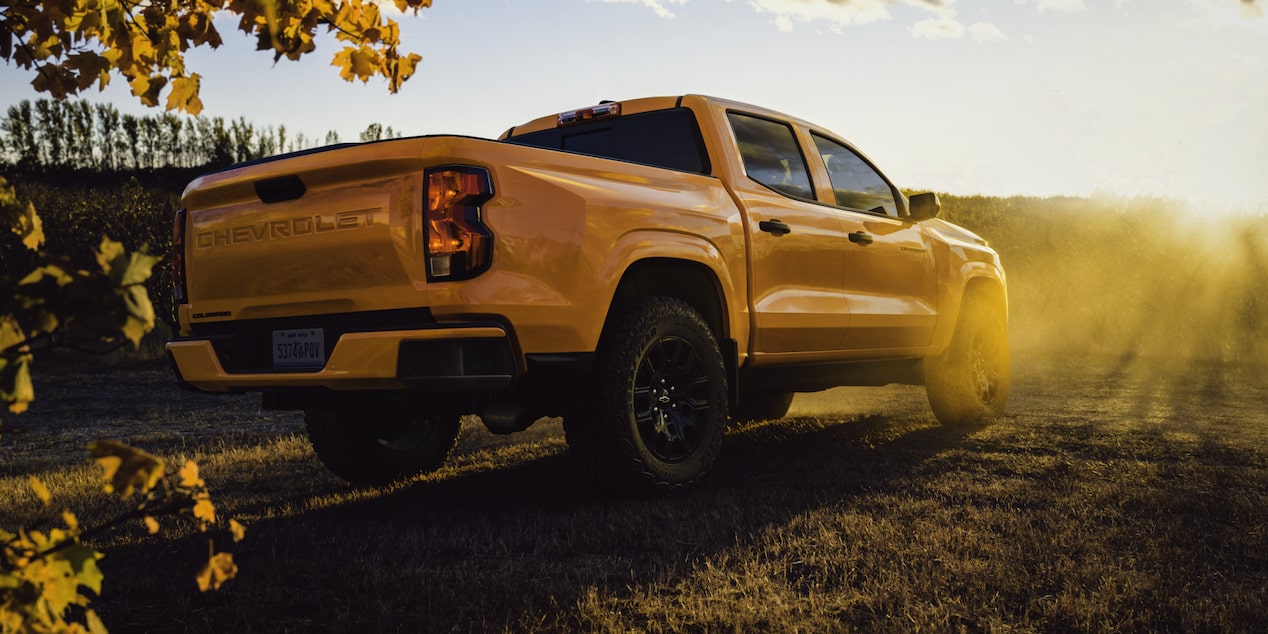 Three Quarters Rear View of a 2026 Yellow Chevy Colorado Facing the Golden Hour Sun on a Grassy Plain