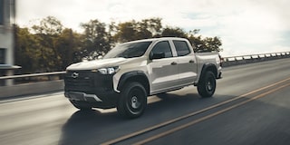 A 2026 Colorado Trail Boss in White Sands equipped with StowFlex Tailgate driving down the highway.