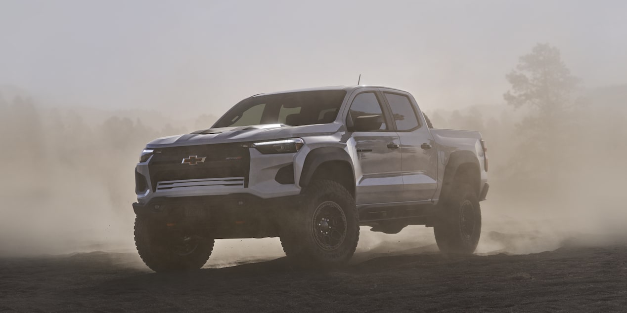 Three Quarters View of a White 2026 Chevy Colorado Driving through a Dust Cloud on a Desert