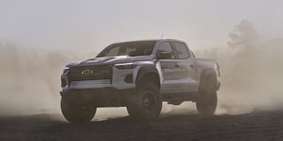 Three Quarters View of a White 2026 Chevy Colorado Driving through a Dust Cloud on a Desert