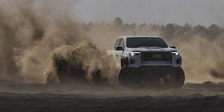 Three Quarters View of a White 2026 Chevy Pickup Truck Driving Though the Desert with Dust and Sand Flying Behind