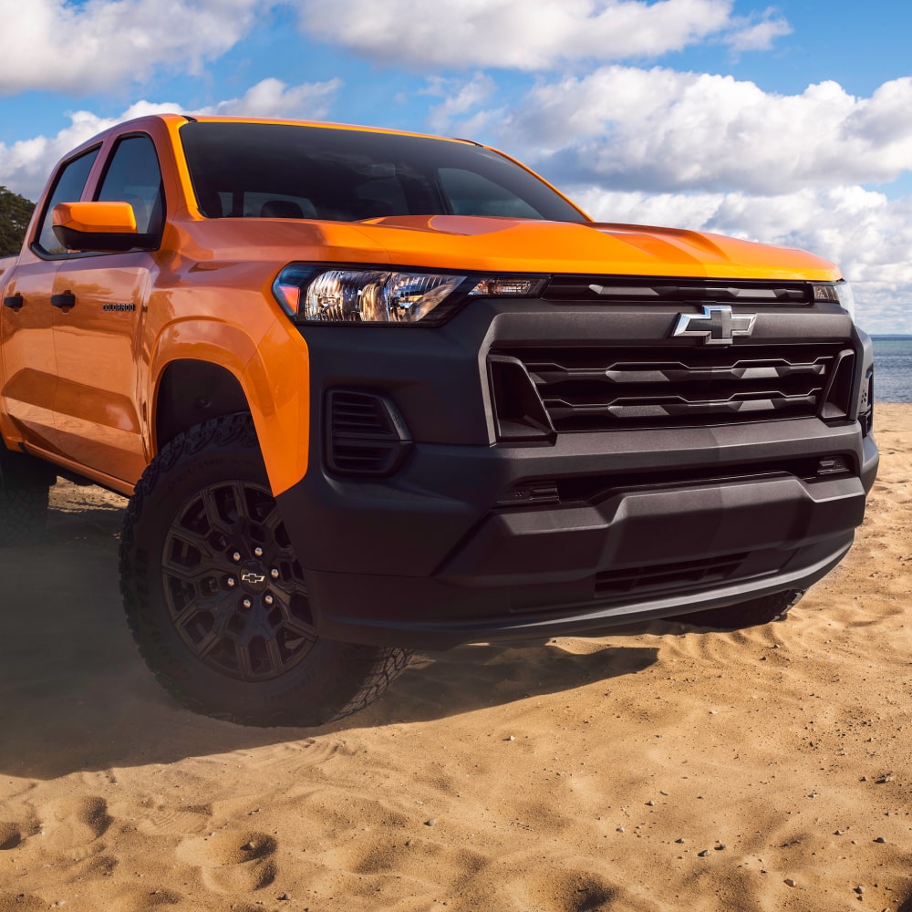 Front View of an Orange 2026 Chevy Colorado Pickup Truck on Sand Next to a Lake