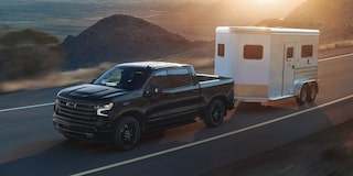 2026 Chevrolet Silverado LD Crew Cab High Country towing an enclosed trailer on the road.