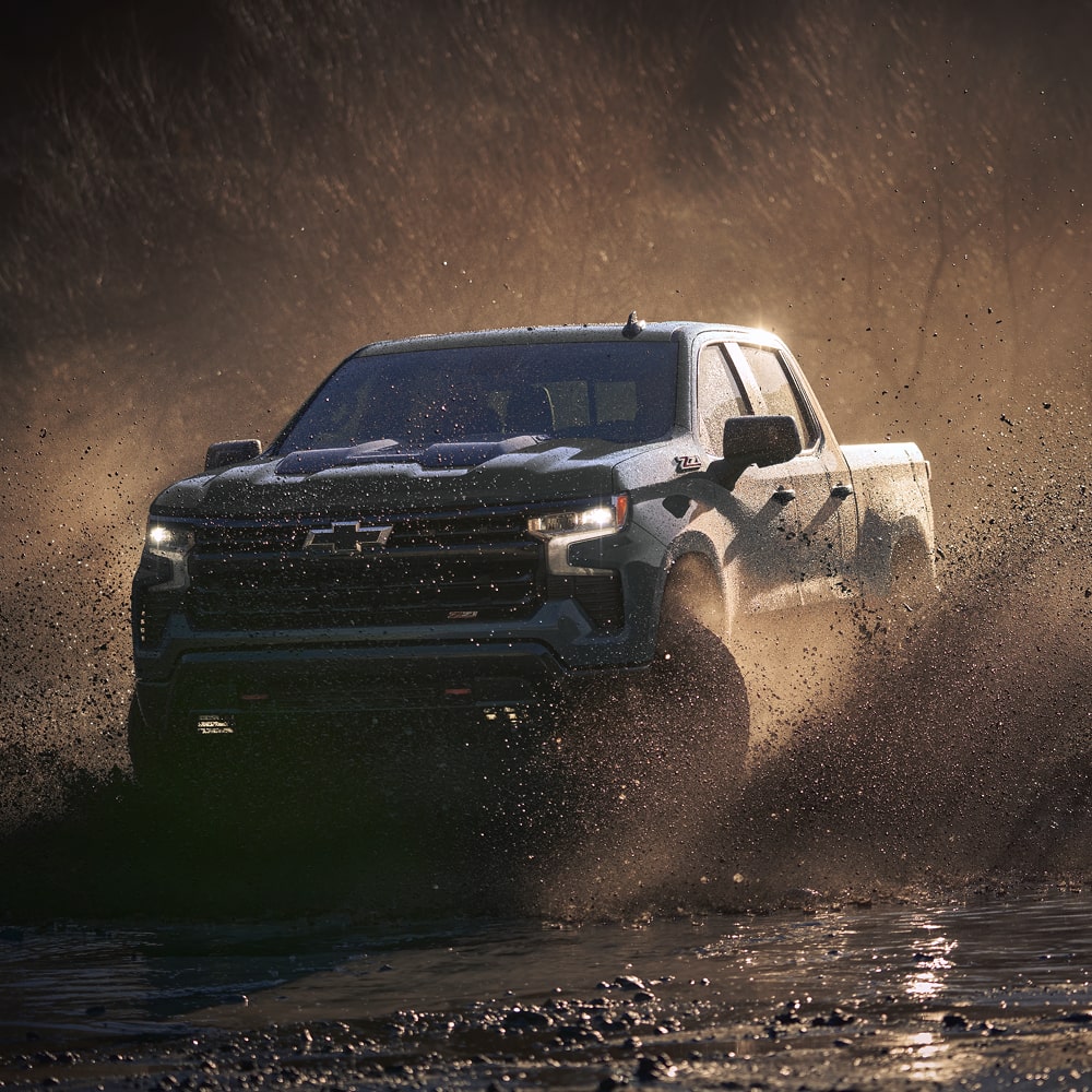 2026 Chevrolet Silverado LD driving off-road on a muddy terrain.