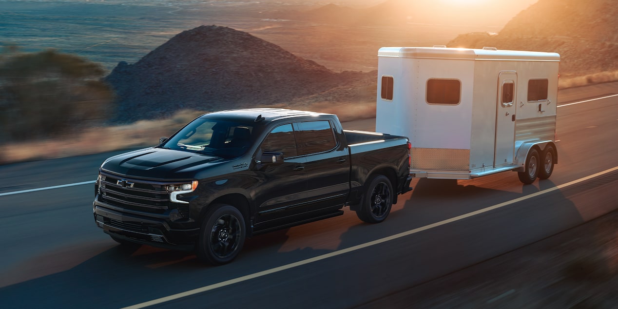 2026 Chevrolet Silverado LD towing a trailer by a beachside road.
