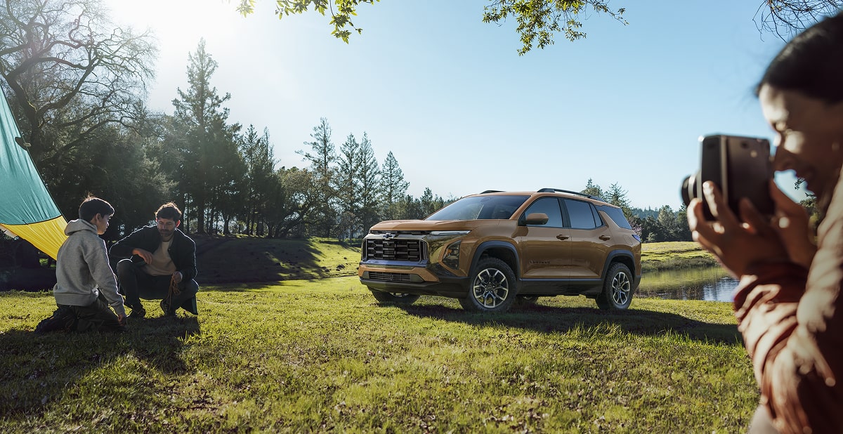 The Sun Shining Down on the Chevy Equinox Parked Outside of a Camping Spot While a Man Takes a Picture of Two Campers