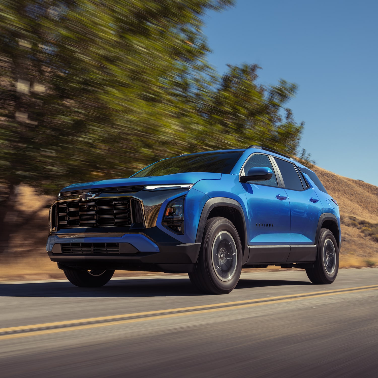 A 2027 Blue Chevy driving down the street line with bushes