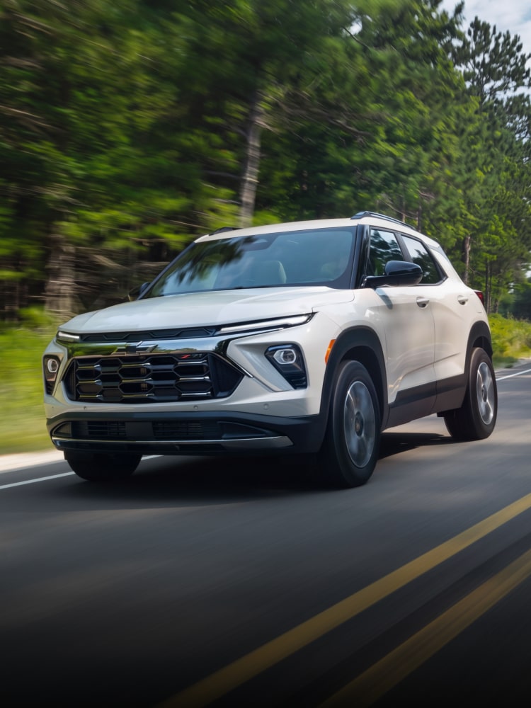 Front View of a 2027 Chevy Trailblazer Driving on a Road Surrounded by Trees