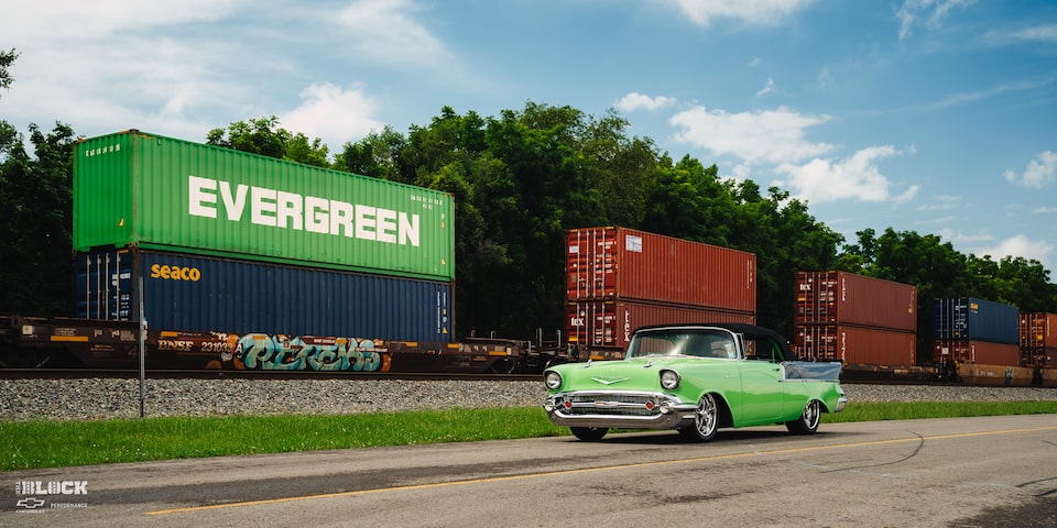A 1957 Chevrolet Convertible Driving On-Road Next to a Train and Tracks