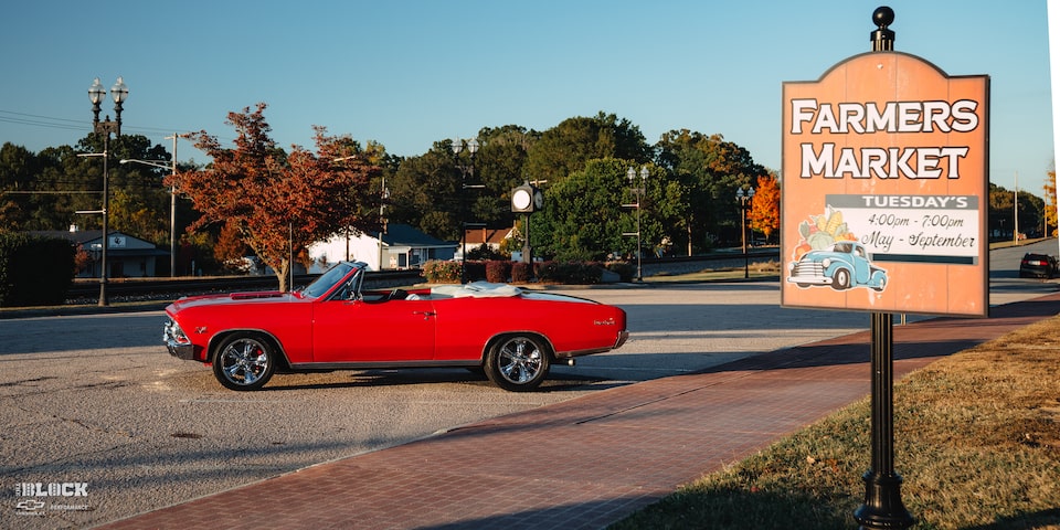 Wide Side View of a 1966 Chevrolet Chevelle SS Convertible Parked in an Empty Parking Lot Next to a Farmers Market Sign