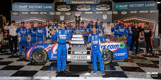 Team Chevy Driver Kyle Larson Posing For a Picture Next to a Trophy With His Team and Vehicle in the Background