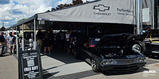 Three Quarters View of a 1969 Black Chevrolet Vehicle with Its Front Hood Open with Many People Around It