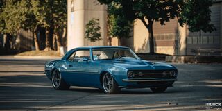 View of a Blue 1968 Chevrolet Camaro Covered by Shade Parked in Front of a Building