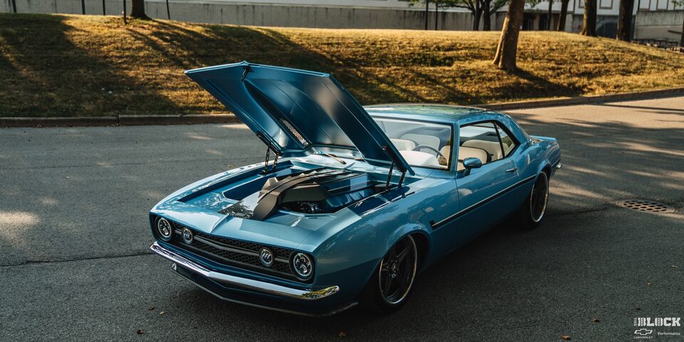 Three Quarters View of a 1968 Blue Chevy Camaro with Its Hood Open on an Empty Road